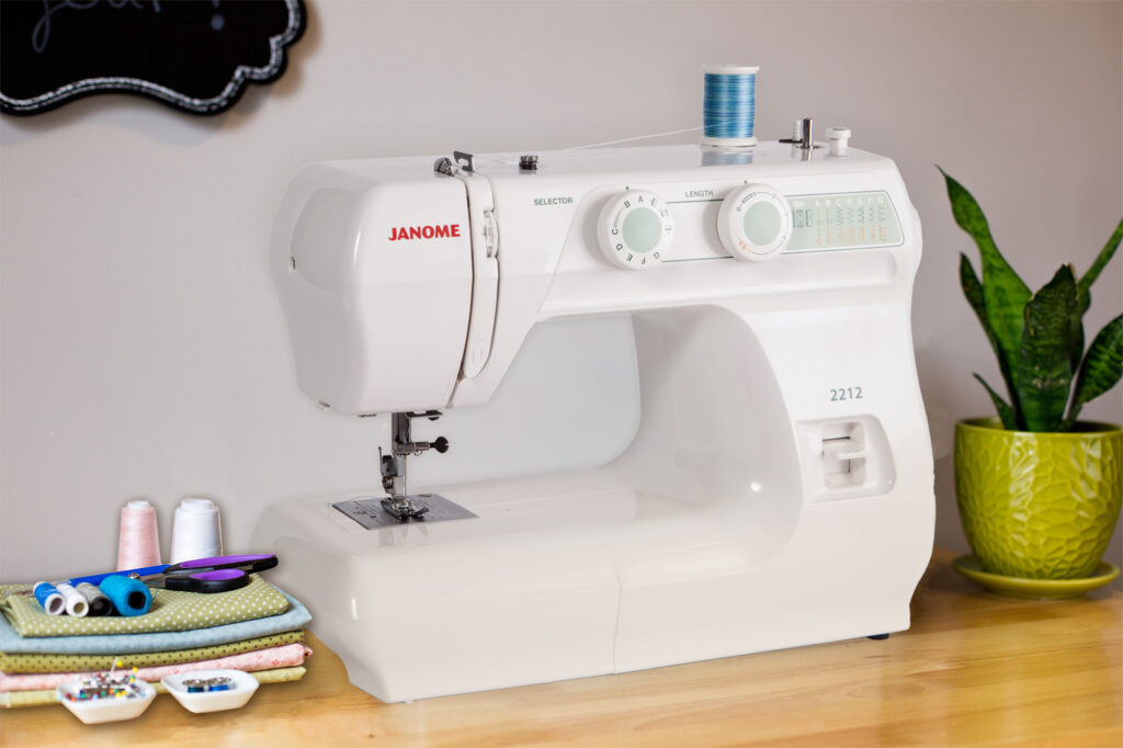 Janome 2212 mechanical sewing machine on a wooden table with thread, fabric, and scissors; dial controls visible. Beginner sewing machine for everyday projects.